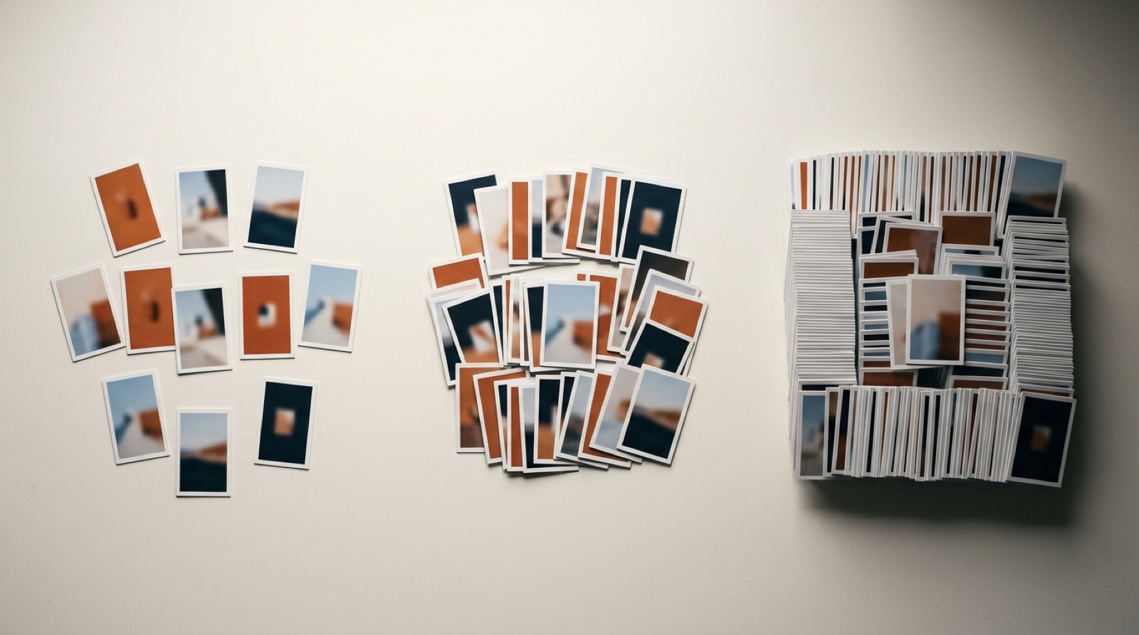 Three groups of small printed ad frame cards laid left to right on a warm white surface, a dozen cards in the first group, several dozen in the second, and a dense block in the third.