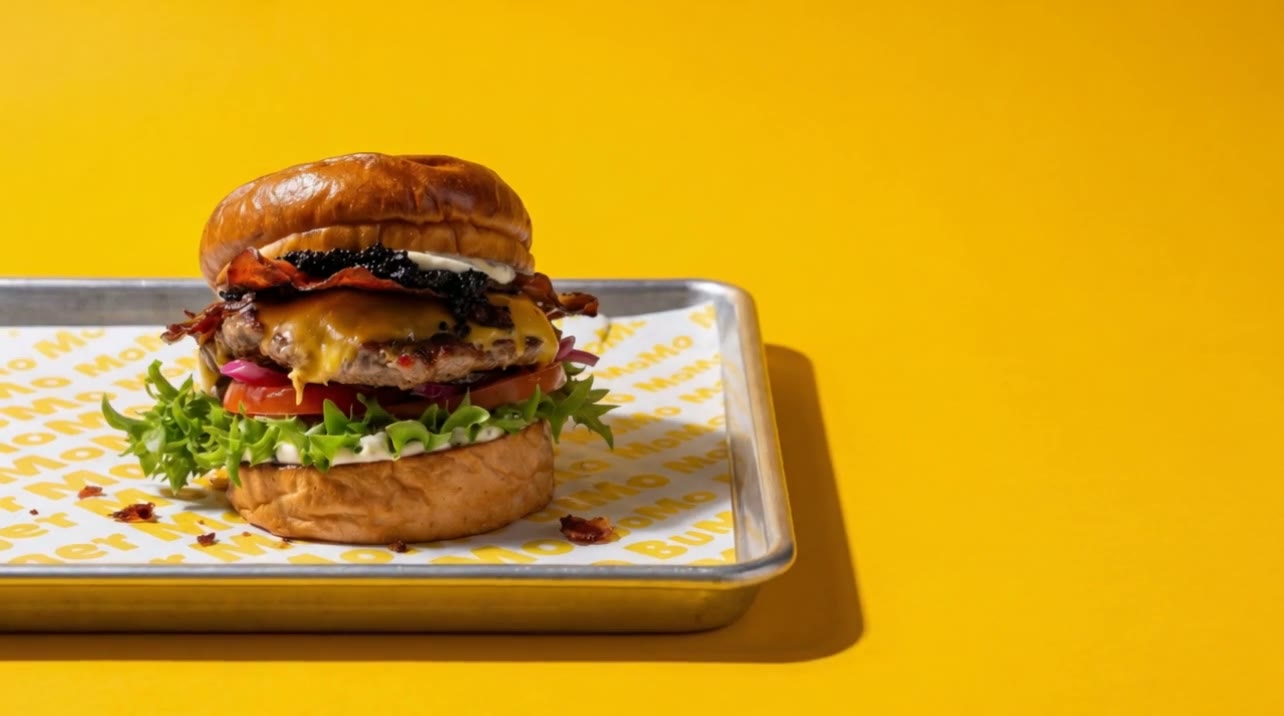 Cinematic macro push in on MoMo's Millionaire burger against a bright yellow backdrop, MoMo tray beneath