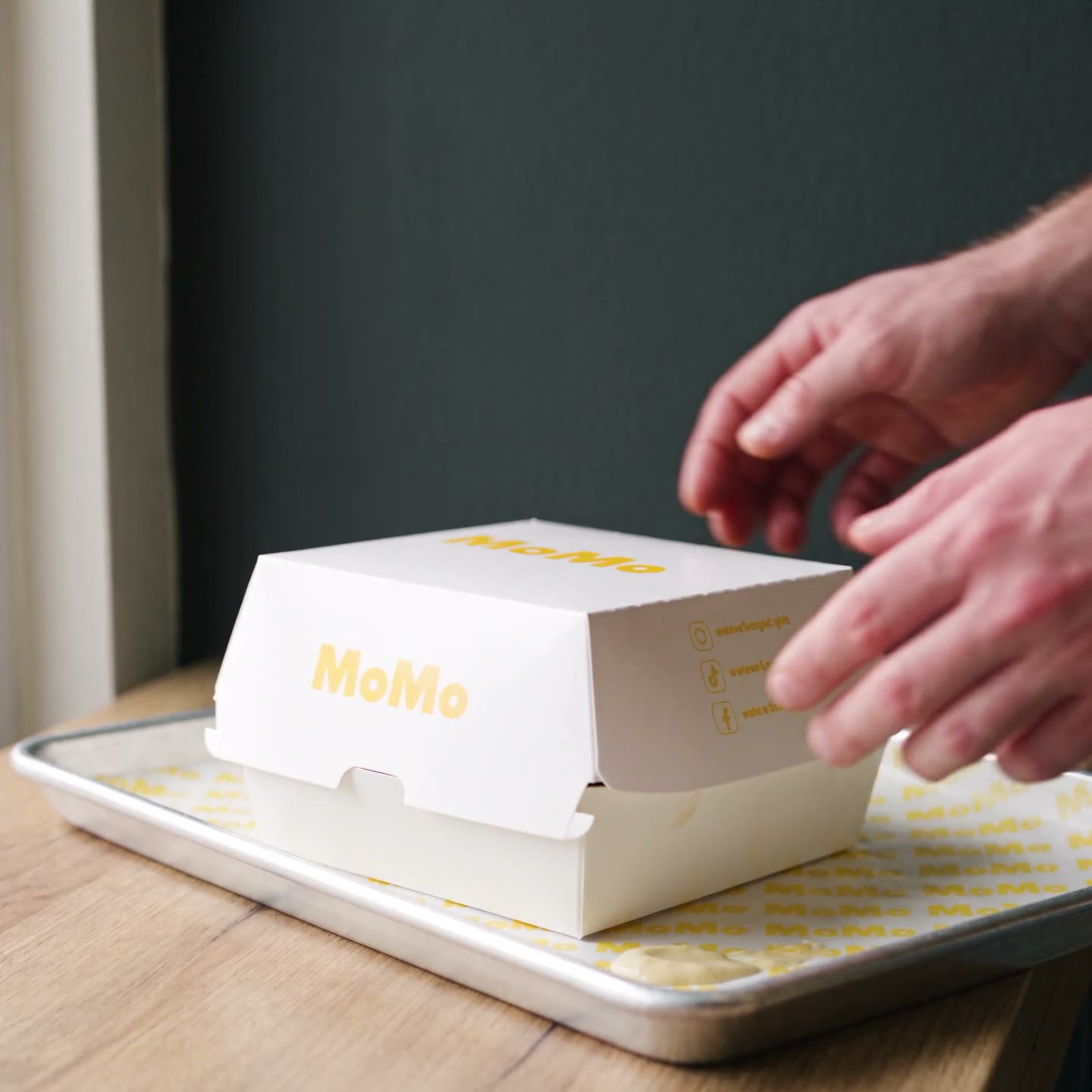 MoMo burger box opening to reveal the bacon and onion ring burger, steam rising, on a MoMo tray