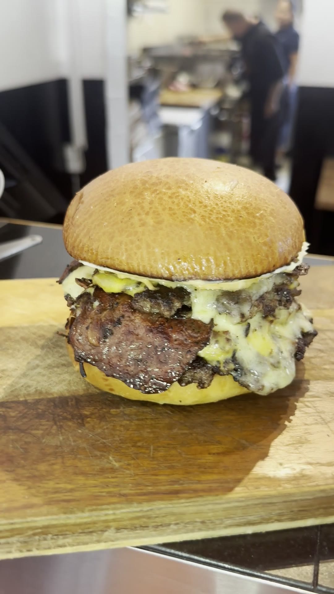 A finished Nordic Smash burger set down on the pass in the kitchen, staff working the line behind it